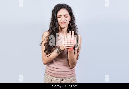 Gestresste hispanische Frau mit Handschmerzen, die vor weißem Hintergrund im Atelier steht Stockfoto
