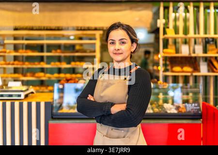 Hispanischer Bäcker mit Schürze, stehend mit gekreuzten Armen in der Bäckerei Stockfoto