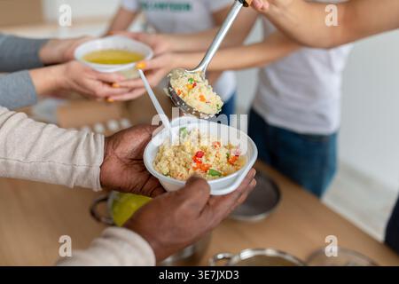 Hände des Schwarzen Mannes, der eine Schüssel Suppe hält, die von einer Gruppe Freiwilliger gegeben wurde, während er in der Mitte steht Stockfoto