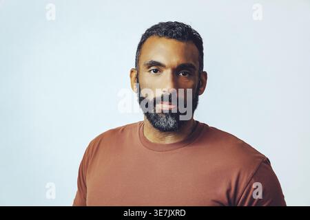 Bärtiger Mann in braunem Hemd, der im Studio an der weißen Wand steht Stockfoto