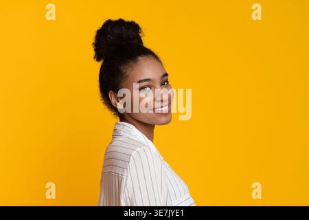 Schwarzer weiblicher Teenager, der seitlich vor gelbem Hintergrund im Studio steht Stockfoto