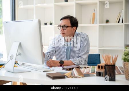 Asiatischer männlicher Innenarchitekt mittleren Alters, der im Büro den Bildschirm ansieht Stockfoto