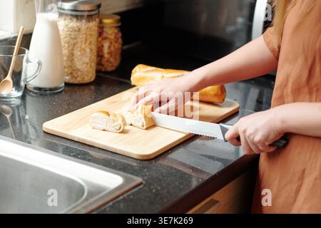 Zugeschnittenes Bild einer asiatischen Frau, die Brot schneidet, die zu Hause an der Küchentheke steht Stockfoto