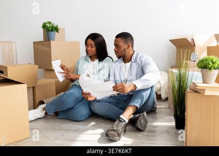 Schwarzes Paar, das im Wohnzimmer zu Hause auf dem Boden zwischen Pappschachteln sitzt Stockfoto