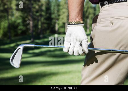 Senior männlicher Golfspieler, der einen Golfschläger hält, der auf einem Golfplatz steht Stockfoto
