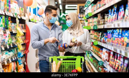 Lächelndes Paar aus dem Nahen Osten, das Gläser hält, während er mit dem Wagen im Supermarkt steht Stockfoto