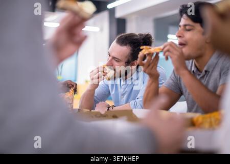 Verschiedene Geschäftsleute essen gemeinsam Pizza, während sie am Tisch sitzen und die Mittagspause im Büro genießen Stockfoto