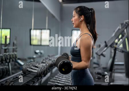 Thailändische Frau in Fitnesskleidung stehend und mit Hanteln im Fitnessstudio trainiert Stockfoto