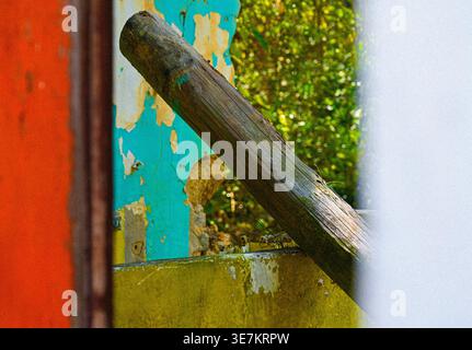 Verwitterter Holzbalken und abblätternde, lackierte Wand mit lebhaften Farben in einem Außenbereich. Stockfoto