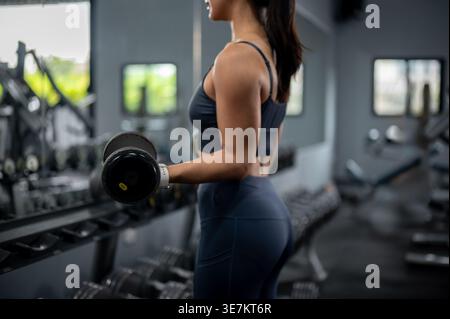 Thailändische Frau in Fitnesskleidung stehend und mit Hanteln im Fitnessstudio trainiert Stockfoto