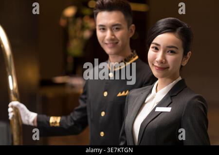 Lächelnde chinesische männliche und weibliche Hotelangestellte stehen in der Hotellobby Stockfoto