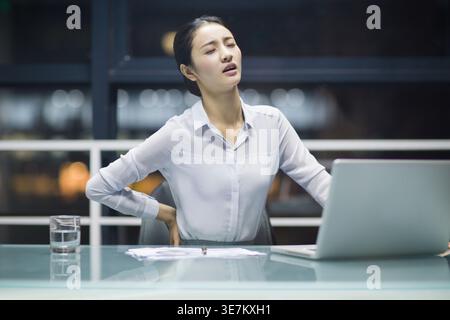 Chinesische Geschäftsfrau mit Rückenschmerzen am Tisch und im Büro Stockfoto