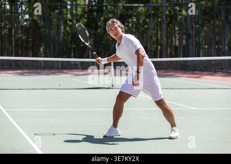 Chinesischer Mann mittleren Alters, der am sonnigen Tag Tennis auf dem Platz spielt Stockfoto
