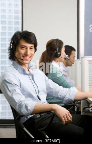 Lächelnder männlicher Call-Center-Agent mit Headset, der am Arbeitsplatz auf dem Stuhl sitzt Stockfoto