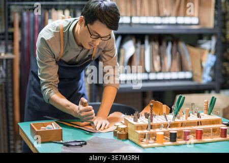 Chinesischer Lederhandwerker, der sich beim Arbeiten am Arbeitsplatz nach vorne lehnt Stockfoto