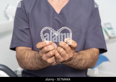 Männlicher Zahnarzt, der Herz mit Aligner in der Zahnklinik zeigt Stockfoto