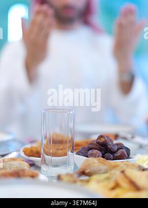 Mann aus dem Nahen Osten, der Kandura trägt, sitzt am Tisch und betet vor dem iftar-Abendessen mit der Familie während des ramadan-Festes zu Hause Stockfoto