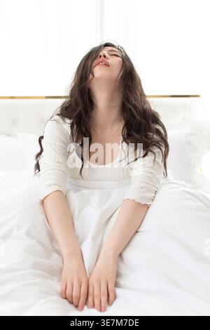 Depressive Chinesin, die den Kopf nach hinten neigt, während sie zu Hause auf dem Bett sitzt Stockfoto