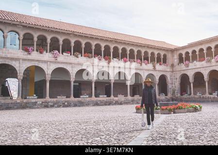 Hispanische Touristenfrau mit Hut und Jacke vor dem Tempel der Sonne der Inkas in Cusco, Peru Stockfoto