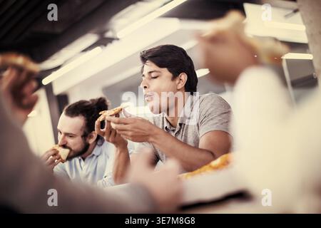 Verschiedene Geschäftsleute essen gemeinsam Pizza, während sie am Tisch sitzen und die Mittagspause im Büro genießen Stockfoto