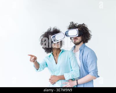 Lächelnde schwarze Frau mit lockigem Afro und kaukasischem Freund, der VR-Headsets trägt und virtuelle Realität erlebt, während er gegen ... dicht beieinander steht Stockfoto