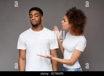 Schwarze Frau streitet mit ihrem nonchalanten Black man Partner vor grauem Hintergrund im Studio Stockfoto