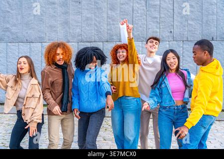 Fröhliche, abwechslungsreiche Gruppe von Freunden, die tagsüber Spaß beim Tanzen in der Nähe der grauen Wand auf der Straße haben Stockfoto