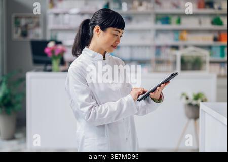 Japanische Apothekerin mit Tablette, die in der Apotheke gegen den Zähler steht Stockfoto