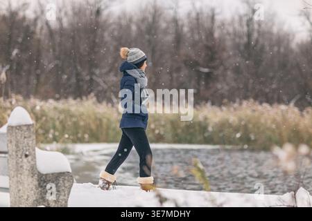 Asiatische Frau, die im schneebedeckten Wald läuft und Teddyjacke und Stiefel trägt Stockfoto