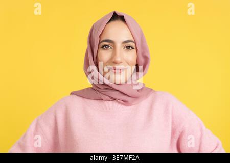Lächelnde muslimische Frau im Hijab, die vor gelbem Hintergrund steht Stockfoto