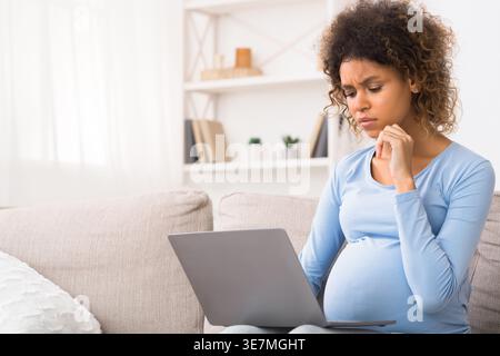 Traurige schwangere Frau mit gemischter Rasse, die zu Hause auf dem Sofa sitzt Stockfoto