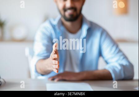Bärtiger Mann aus dem Nahen Osten, der sich mit Papier am Tisch sitzend im Wohnzimmer zu Hause anbietet Stockfoto