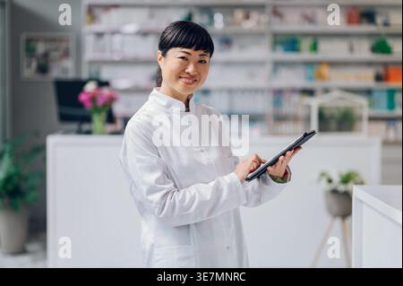 Japanische Apothekerin mit Tablette, die in der Apotheke gegen den Zähler steht Stockfoto