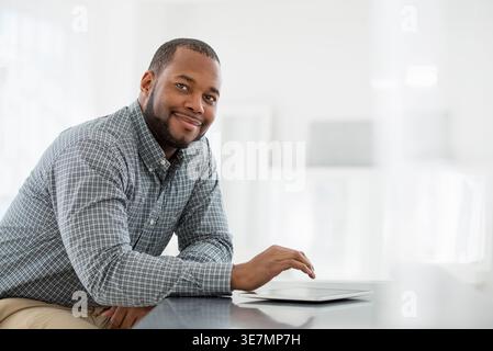 Lächelnder afroamerikanischer Geschäftsmann, der am Tisch mit Tablet im Büro sitzt Stockfoto