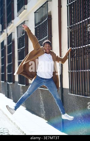 Schwarzer Mann, der sich an Fenstergittern festhält und an sonnigem Tag auf der Straße springt Stockfoto