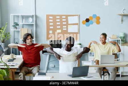 Gruppe von IT-Spezialisten, die Dehnübungen durchführen, während sie am Tisch im Büro sitzen Stockfoto