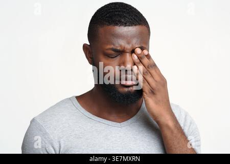 Schwarzer Mann reibt sich das Auge, während er im Studio vor weißem Hintergrund steht Stockfoto