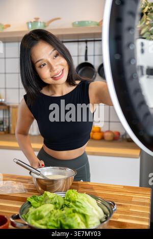 Asiatische Food Bloggerin nimmt sich auf, während sie gesundes Gericht in der Küche zubereitet Stockfoto
