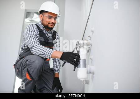 Indischer Klempner mit Uniform und Schutzhelm, der Wasserausrüstung im Badezimmer installiert Stockfoto