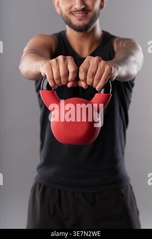 Asiatischer Mann hebt Kettlebell, während er vor grauem Hintergrund im Studio steht Stockfoto