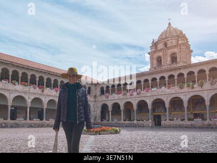 Hispanische Touristenfrau mit Hut und Jacke vor dem Tempel der Sonne der Inkas in Cusco, Peru Stockfoto