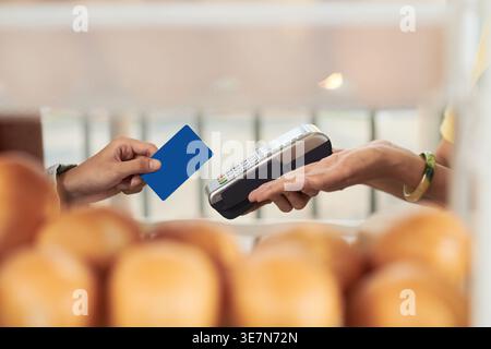 Zugeschnittenes Bild einer vietnamesischen Barista, die das POS-Terminal hält und Kreditkartenzahlungen von Kunden akzeptiert, während sie am Schalter im Café stehen Stockfoto