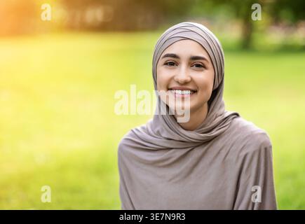 Fröhliche arabische Frau im Hijab, die tagsüber im Park sitzt Stockfoto