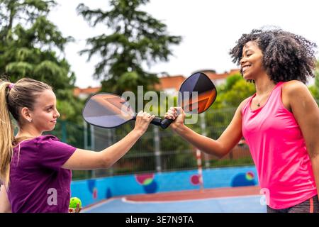 Viele weibliche Freunde, die tagsüber gegen Schläger kämpfen, bevor sie auf dem Hof pickleball spielen Stockfoto