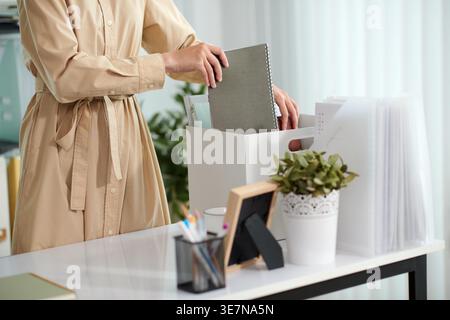 Zugeschnittenes Bild einer asiatischen Geschäftsfrau, die Dokumente aus der Schachtel im Büro auf ihren Schreibtisch bringt Stockfoto