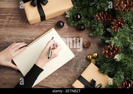 Hände einer asiatischen Frau, die zu Hause einen Brief mit eingewickelten Geschenken auf den Tisch schreibt Stockfoto
