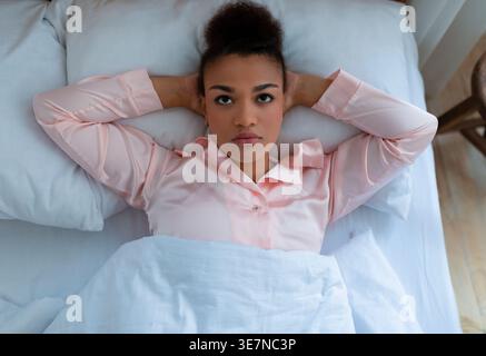 Deprimierte schwarze Frau mit Händen hinter dem Kopf, die zu Hause auf dem Bett liegen Stockfoto