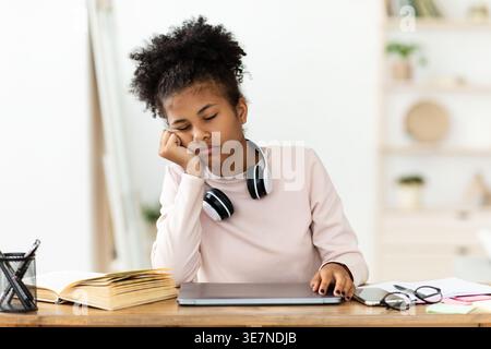Müde Schwarzes Jungmädchen schlafend liegendes Gesicht auf der Hand sitzend am Tisch mit Laptop zu Hause Stockfoto
