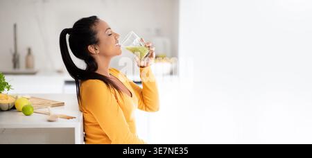 Schwarze Frau mit geschlossenen Augen, die Smoothie trinkt, während sie zu Hause am Tisch in der Küche steht Stockfoto