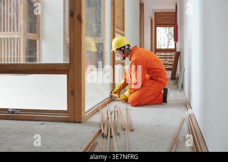 Männlicher Bauarbeiter mit gemischter Rasse, der Holzfensterrahmen beim Knien auf der Baustelle installiert Stockfoto